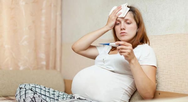 This may contain: a pregnant woman sitting on a couch holding a toothbrush and looking at her forehead