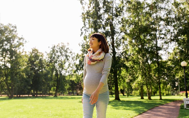 This may contain: a pregnant woman is standing in the park